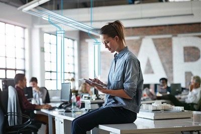 Osoba korzystająca z tabletu w nowoczesnym biurze z naturalnym oświetleniem i pracującymi w tle kolegami z pracy