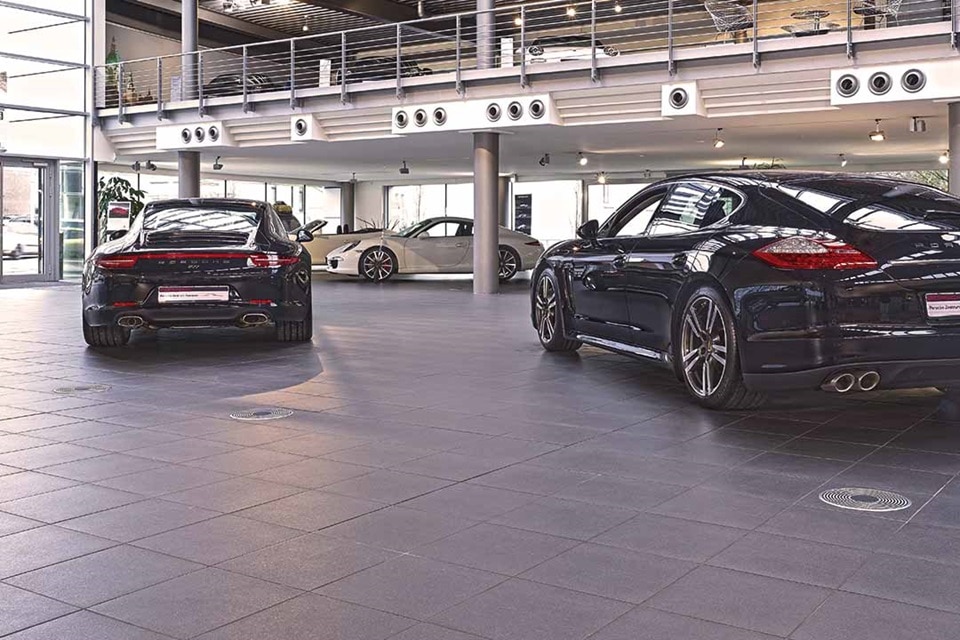 Carros de luxo expostos em uma concessionária moderna com grandes janelas e iluminação industrial no teto