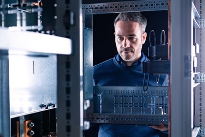 Técnico inspecionando armário elétrico com trilhos de montagem de disjuntores em ambiente industrial