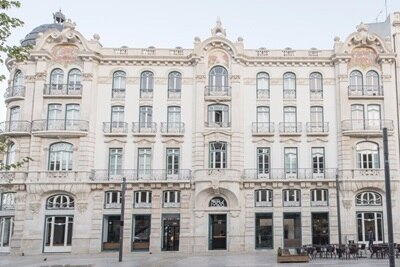 Fachada de um edifício histórico com arquitetura ornamentada e assentos ao ar livre à frente