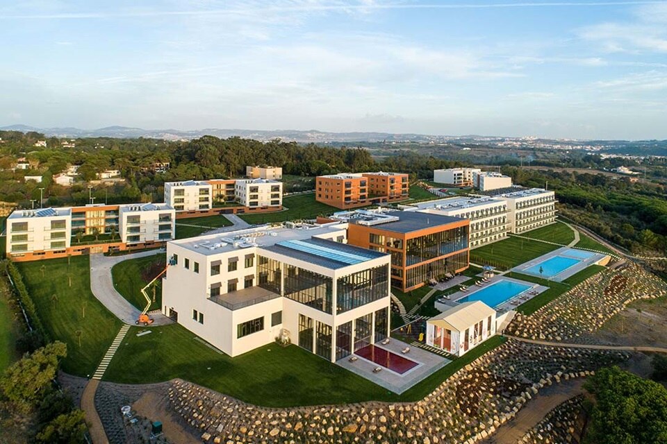 Vista aérea de uma área residencial e comercial moderna com edifícios, piscinas e jardins paisagísticos
