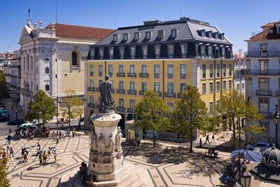 Vista aérea de uma praça movimentada com uma estátua, edifícios históricos e pedestres em Lisboa, Portugal