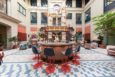 Elegant atriumlounge i ett modernt hotell med en bardisk i centrum, hängande glaslampor och mönstrat golv