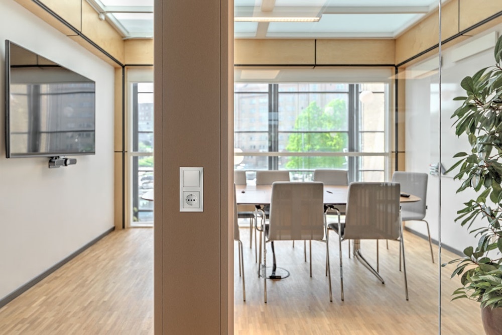 Modernt kontorsinteriör med väggmonterat eluttag och ljusströmbrytare på en pelare med ett konferensrum i bakgrunden