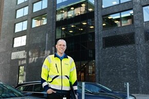 Person i hög synlighet väst står framför en kontorsbyggnad