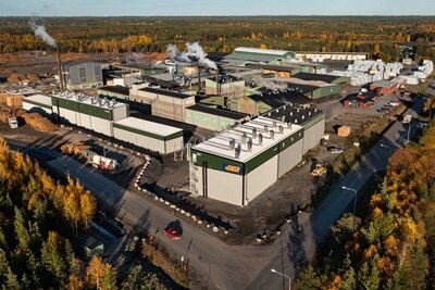 Flygbild av ett industriellt anläggning med flera byggnader omgivna av höstlöv