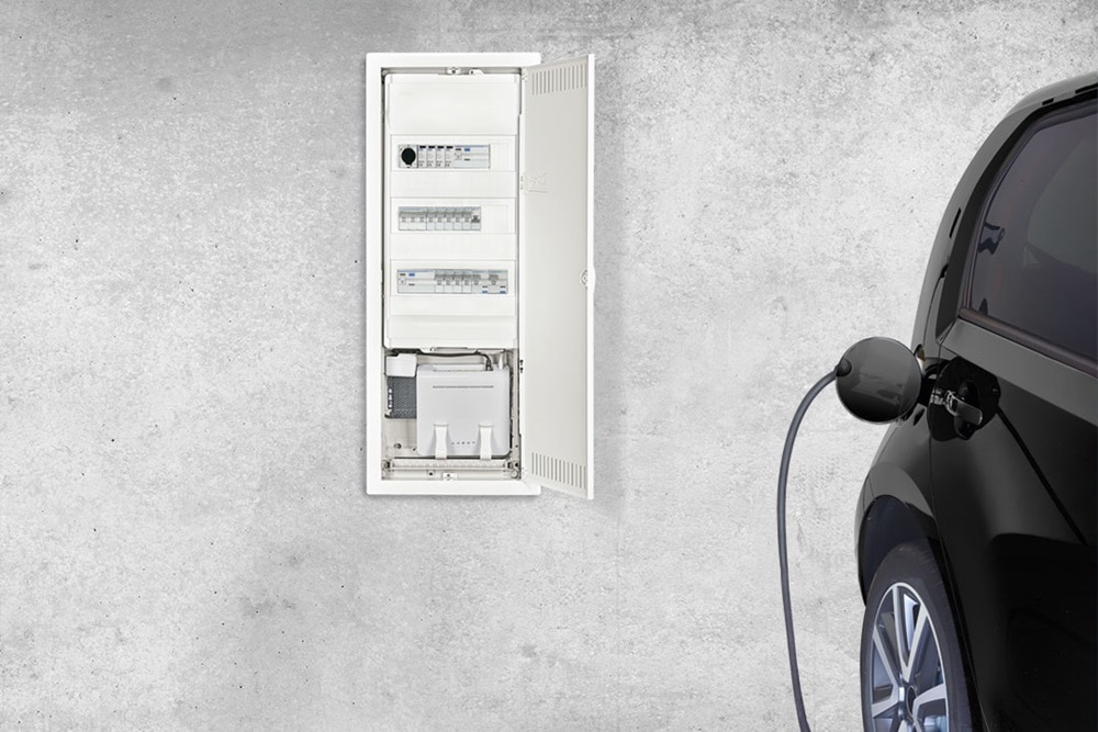Elbil ansluten till en laddbox bredvid en öppen elcentral på en betongvägg