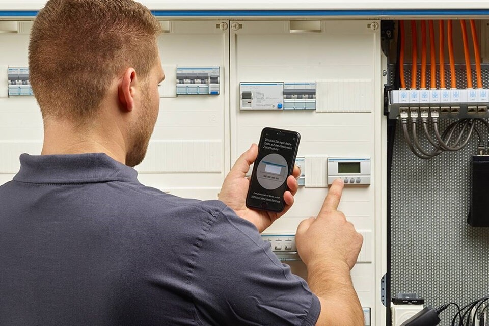 Tekniker använder en smartphone för att konfigurera ett system för smart hemautomation nära elektriska fördelningstavlor