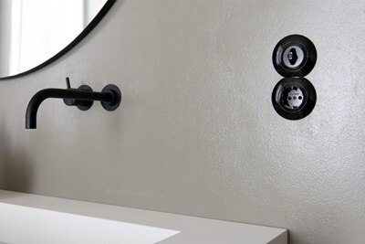 Svart strömställare serie 1930 från Hager monterat på en grå vägg