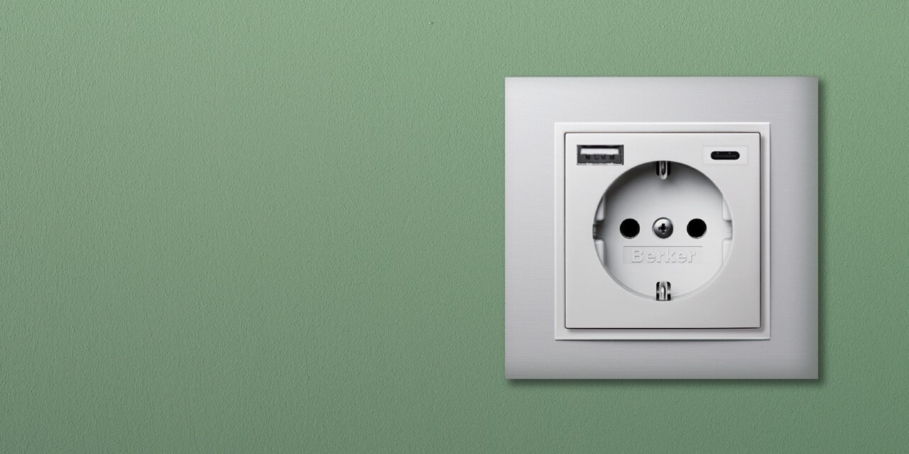Moderne Wandsteckdose mit integrierten USB-Anschlüssen von Berker an einer grünen Wand